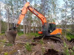 Kaivinkone kaivutyössä metsässä järven rannalla